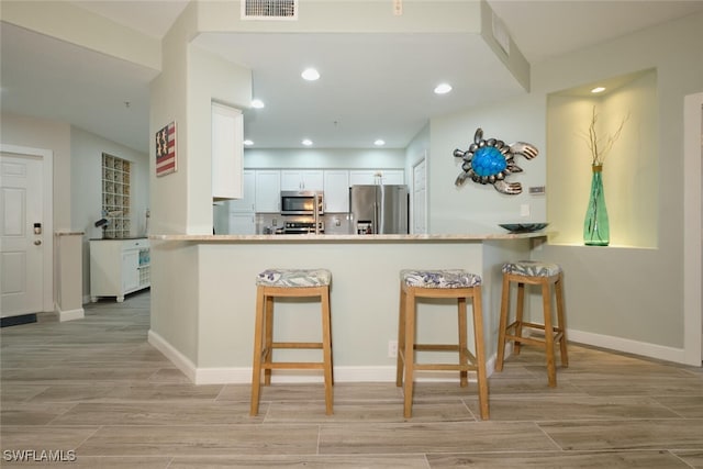 kitchen featuring kitchen peninsula, a breakfast bar area, white cabinetry, light hardwood / wood-style floors, and stainless steel appliances