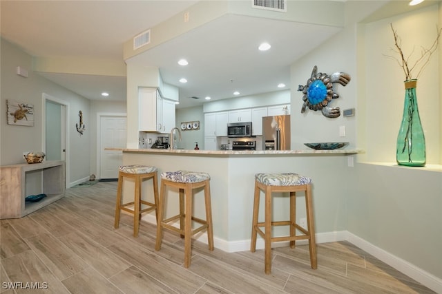 kitchen with a kitchen bar, kitchen peninsula, stainless steel appliances, white cabinets, and light hardwood / wood-style flooring