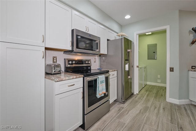 kitchen with appliances with stainless steel finishes, white cabinetry, light hardwood / wood-style flooring, washing machine and dryer, and light stone counters