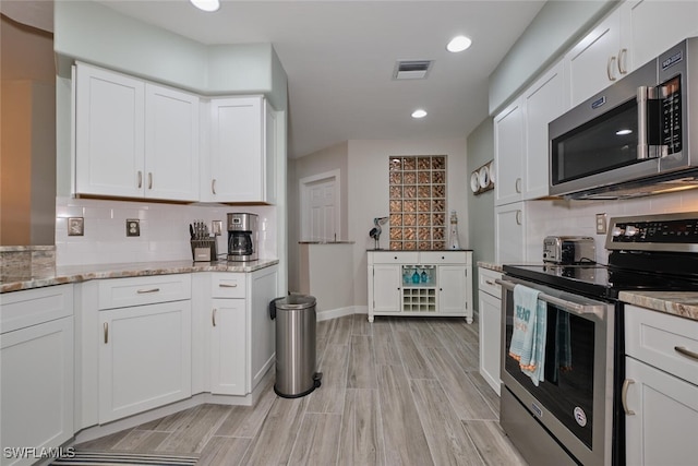 kitchen featuring tasteful backsplash, light stone counters, white cabinetry, light hardwood / wood-style floors, and stainless steel appliances