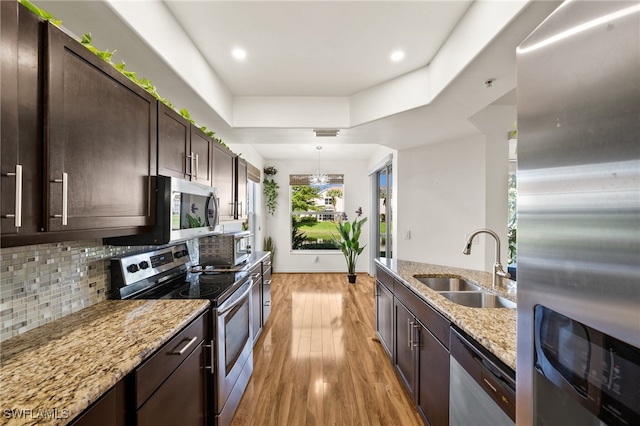 kitchen featuring appliances with stainless steel finishes, light wood-type flooring, light stone counters, dark brown cabinets, and sink