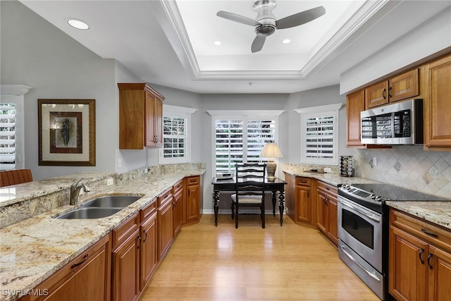 kitchen featuring stainless steel appliances, light hardwood / wood-style floors, sink, backsplash, and a tray ceiling