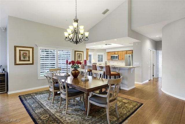 dining area featuring high vaulted ceiling, beverage cooler, a chandelier, and light hardwood / wood-style flooring