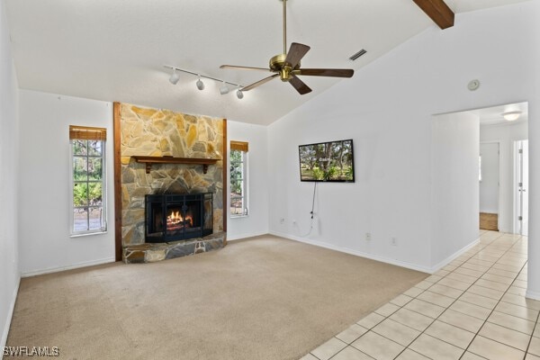 unfurnished living room with track lighting, light colored carpet, ceiling fan, lofted ceiling with beams, and a fireplace