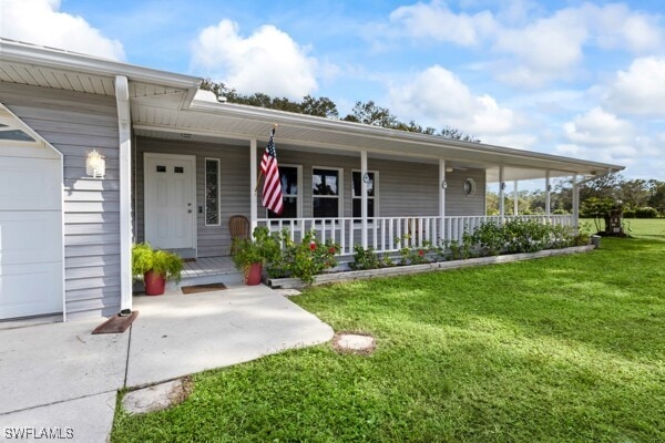 view of exterior entry featuring covered porch, a garage, and a lawn