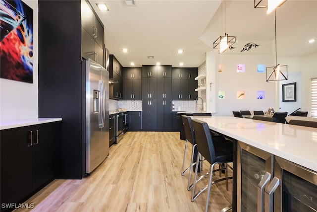 kitchen with a kitchen bar, backsplash, light hardwood / wood-style floors, stainless steel appliances, and pendant lighting