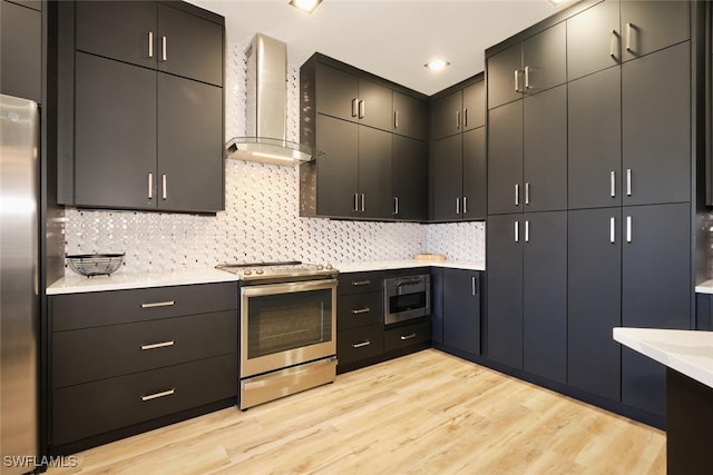 kitchen with appliances with stainless steel finishes, tasteful backsplash, wall chimney range hood, and light hardwood / wood-style floors