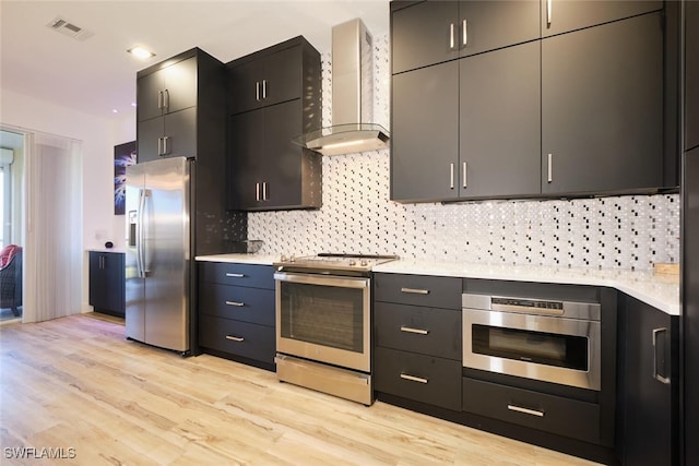 kitchen featuring appliances with stainless steel finishes, wall chimney exhaust hood, decorative backsplash, and light wood-type flooring