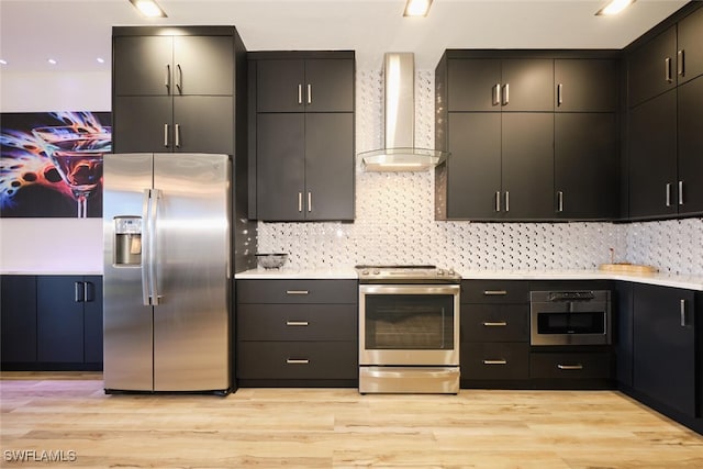 kitchen featuring backsplash, wall chimney exhaust hood, appliances with stainless steel finishes, and light wood-type flooring