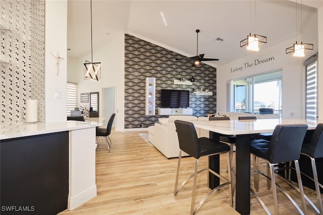 dining space featuring ornamental molding, light hardwood / wood-style flooring, a towering ceiling, and ceiling fan