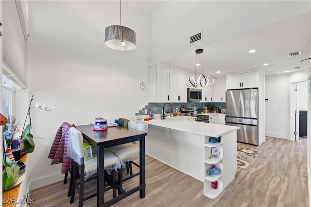 kitchen with light hardwood / wood-style floors, kitchen peninsula, white cabinets, and stainless steel appliances