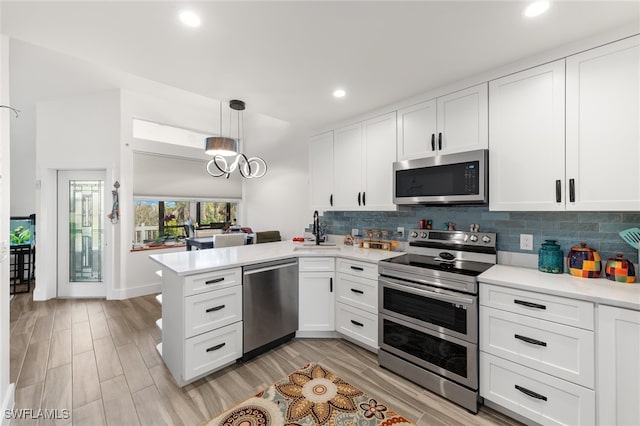 kitchen with appliances with stainless steel finishes, sink, kitchen peninsula, pendant lighting, and white cabinets