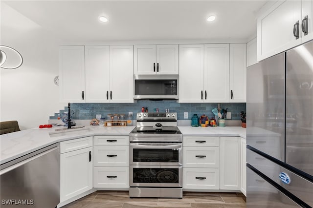 kitchen featuring kitchen peninsula, stainless steel appliances, light stone countertops, white cabinetry, and tasteful backsplash