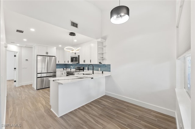 kitchen with light wood-type flooring, kitchen peninsula, hanging light fixtures, stainless steel appliances, and white cabinets