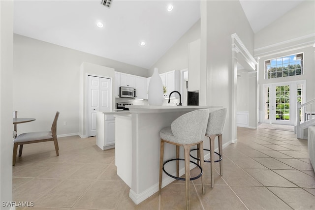 kitchen with kitchen peninsula, white cabinetry, light tile patterned floors, appliances with stainless steel finishes, and high vaulted ceiling