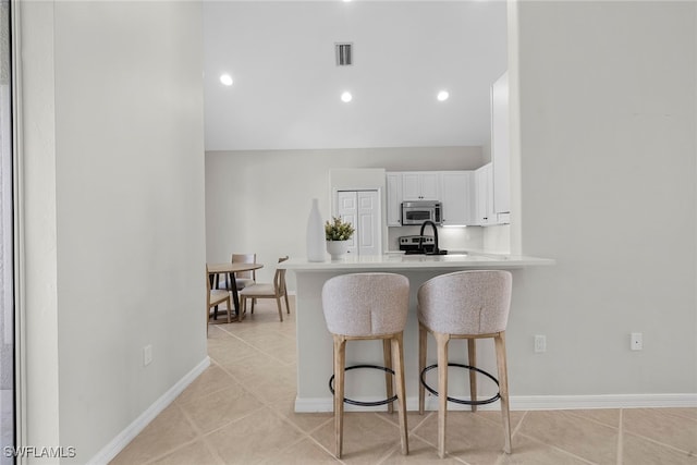 kitchen featuring stainless steel appliances, kitchen peninsula, a kitchen breakfast bar, and white cabinets