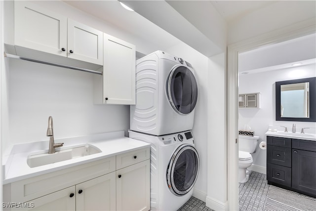 clothes washing area with sink, stacked washer and clothes dryer, light tile patterned floors, and cabinets