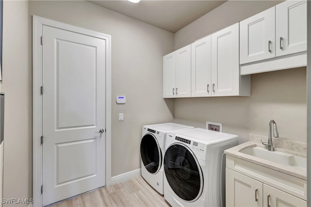 laundry area featuring cabinets, light wood-type flooring, washing machine and clothes dryer, and sink