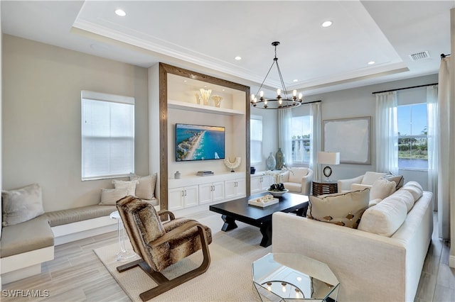 living room with a notable chandelier, a tray ceiling, and light hardwood / wood-style floors