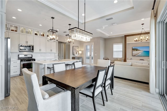 dining area with ornamental molding, a tray ceiling, light hardwood / wood-style floors, and sink