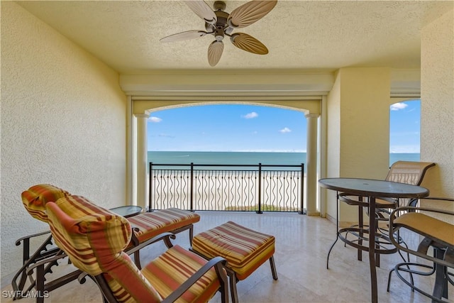 balcony with a beach view, ceiling fan, and a water view