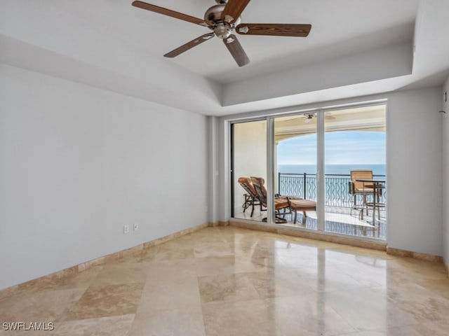 empty room featuring a water view, ceiling fan, and a tray ceiling