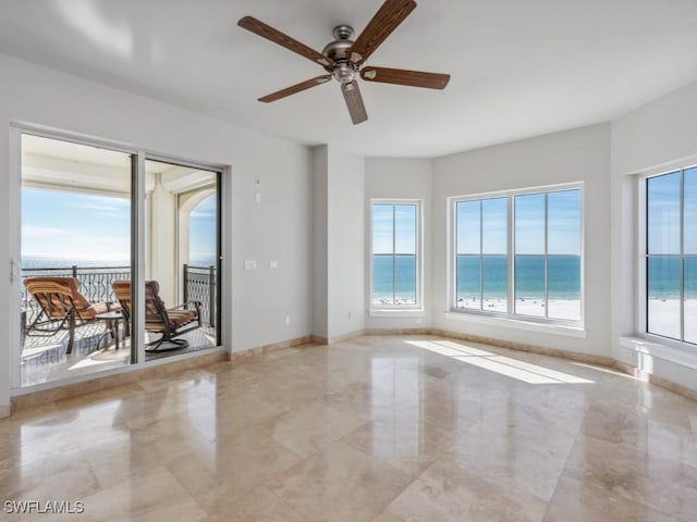 unfurnished room with a water view, plenty of natural light, ceiling fan, and a view of the beach