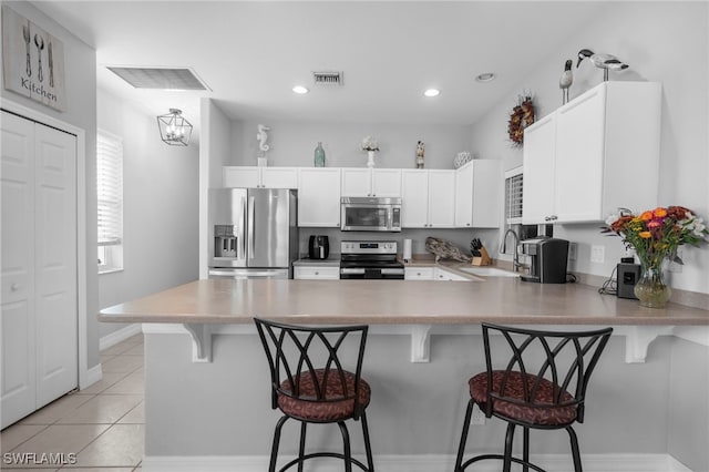 kitchen featuring sink, kitchen peninsula, white cabinetry, stainless steel appliances, and a breakfast bar