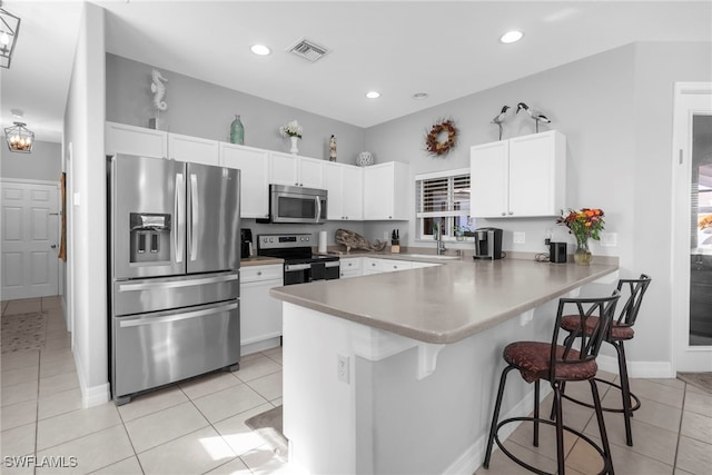 kitchen with appliances with stainless steel finishes, a breakfast bar, kitchen peninsula, white cabinets, and light tile patterned floors