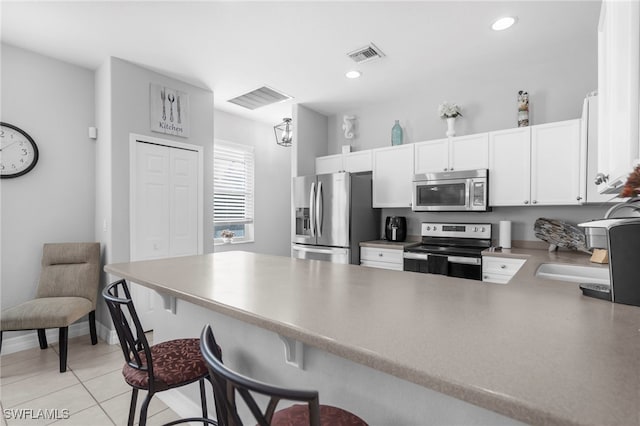 kitchen with kitchen peninsula, a breakfast bar area, appliances with stainless steel finishes, light tile patterned floors, and white cabinetry