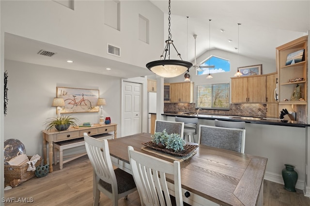 dining space featuring sink, light hardwood / wood-style flooring, and high vaulted ceiling