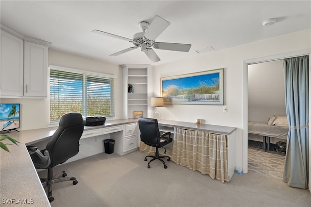 carpeted home office with built in desk and ceiling fan