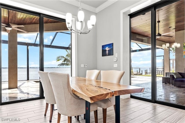 dining area featuring light hardwood / wood-style flooring, ceiling fan with notable chandelier, a wall of windows, and a water view