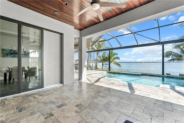 view of pool with ceiling fan, a patio area, glass enclosure, and a water view