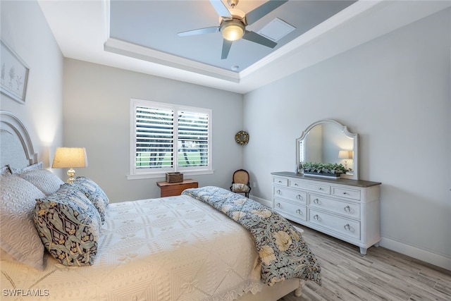 bedroom with a raised ceiling, ceiling fan, and light hardwood / wood-style flooring