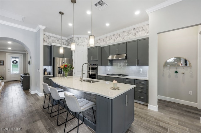 kitchen with stainless steel appliances, hanging light fixtures, sink, an island with sink, and gray cabinetry