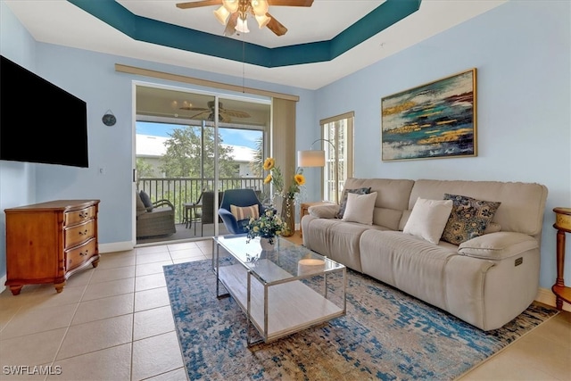 tiled living room with ceiling fan and a raised ceiling