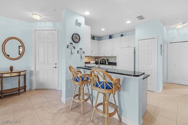 kitchen with white refrigerator, a breakfast bar area, white cabinets, and light tile patterned flooring