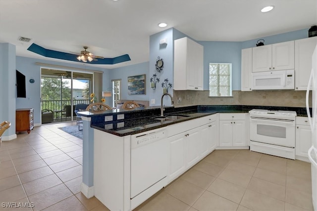 kitchen with white appliances, kitchen peninsula, white cabinets, dark stone counters, and sink