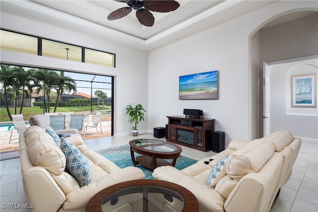 tiled living room with a tray ceiling, ceiling fan, and a fireplace