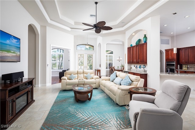 living room featuring light tile patterned flooring, ceiling fan, crown molding, and a tray ceiling