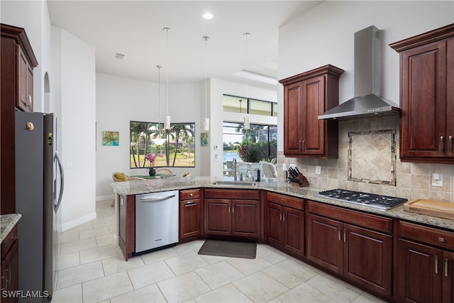 kitchen featuring light stone counters, stainless steel appliances, pendant lighting, sink, and wall chimney exhaust hood