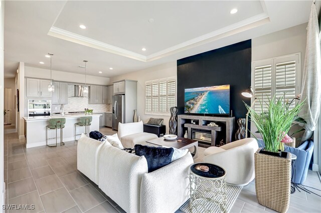 living room with light tile patterned flooring, a tray ceiling, a wealth of natural light, and sink