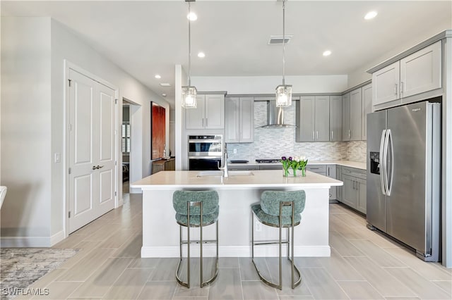 kitchen with appliances with stainless steel finishes, gray cabinets, hanging light fixtures, and an island with sink