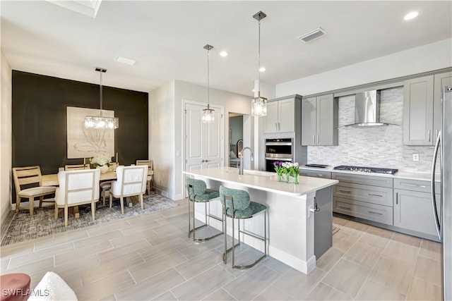 kitchen with a kitchen island with sink, wall chimney exhaust hood, pendant lighting, and appliances with stainless steel finishes