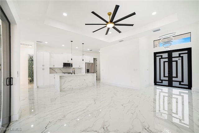 unfurnished living room featuring a tray ceiling, ceiling fan, and sink