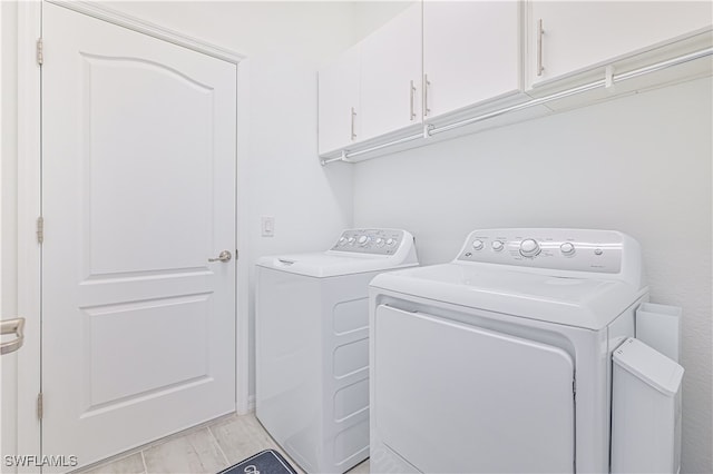 clothes washing area featuring light hardwood / wood-style flooring, cabinets, and washer and dryer