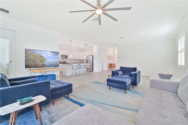 living room with light hardwood / wood-style floors, ceiling fan, sink, and crown molding