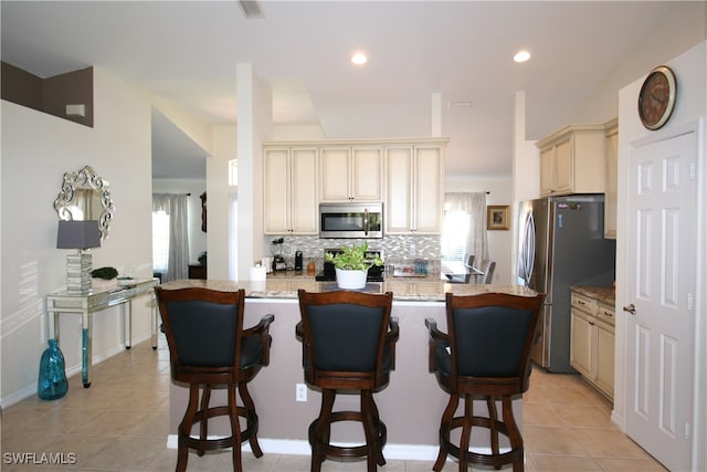 kitchen featuring appliances with stainless steel finishes, cream cabinetry, and a kitchen bar