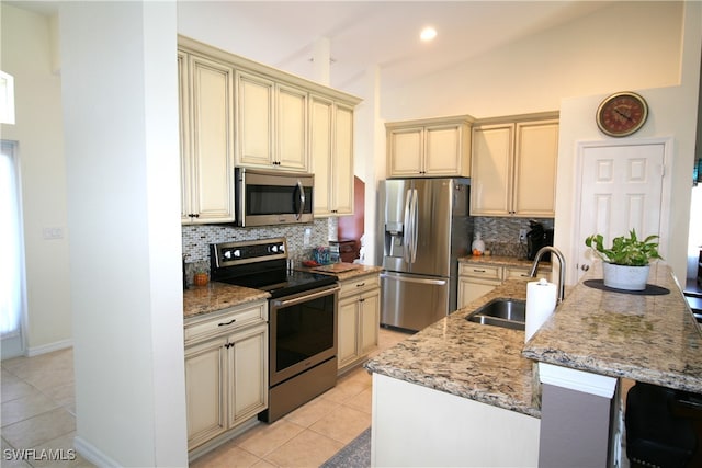 kitchen with an island with sink, appliances with stainless steel finishes, vaulted ceiling, cream cabinetry, and sink